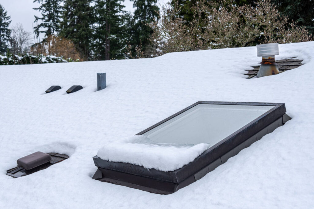Roof vents and window viewed from the outside; snow covering most of the surface