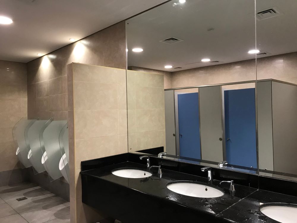  Toilet cubicles reflecting in big beveled mirrors black granite wash basin counter soap dispenser and urinals