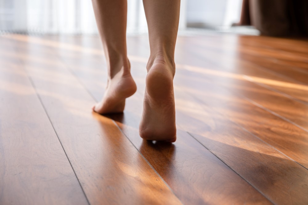 Woman walking barefoot on toes at warm laminate floor close up rear view