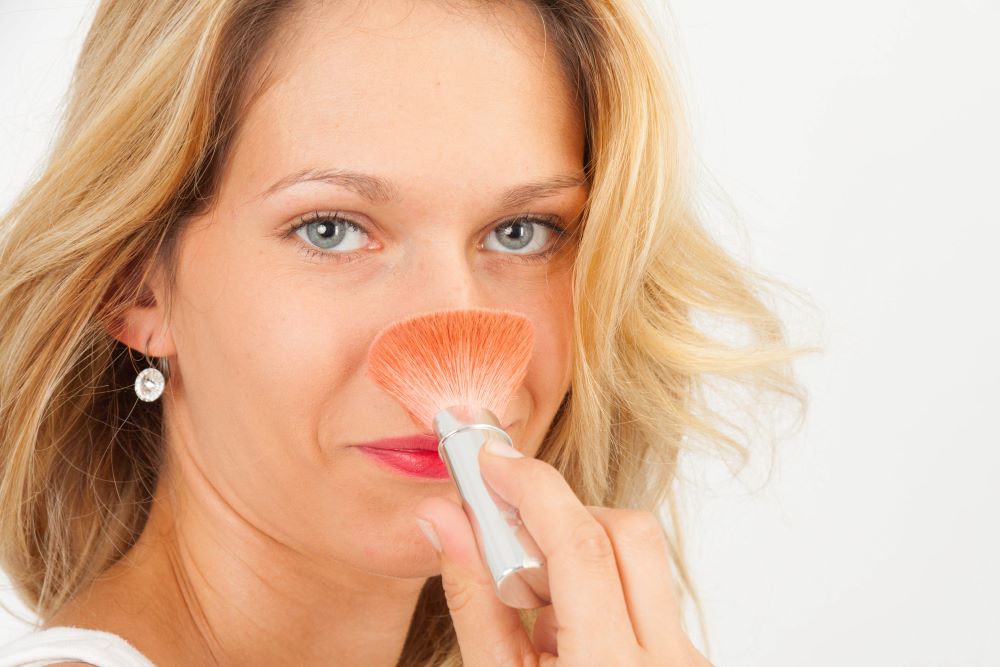 Woman with powder brush powdering her nose