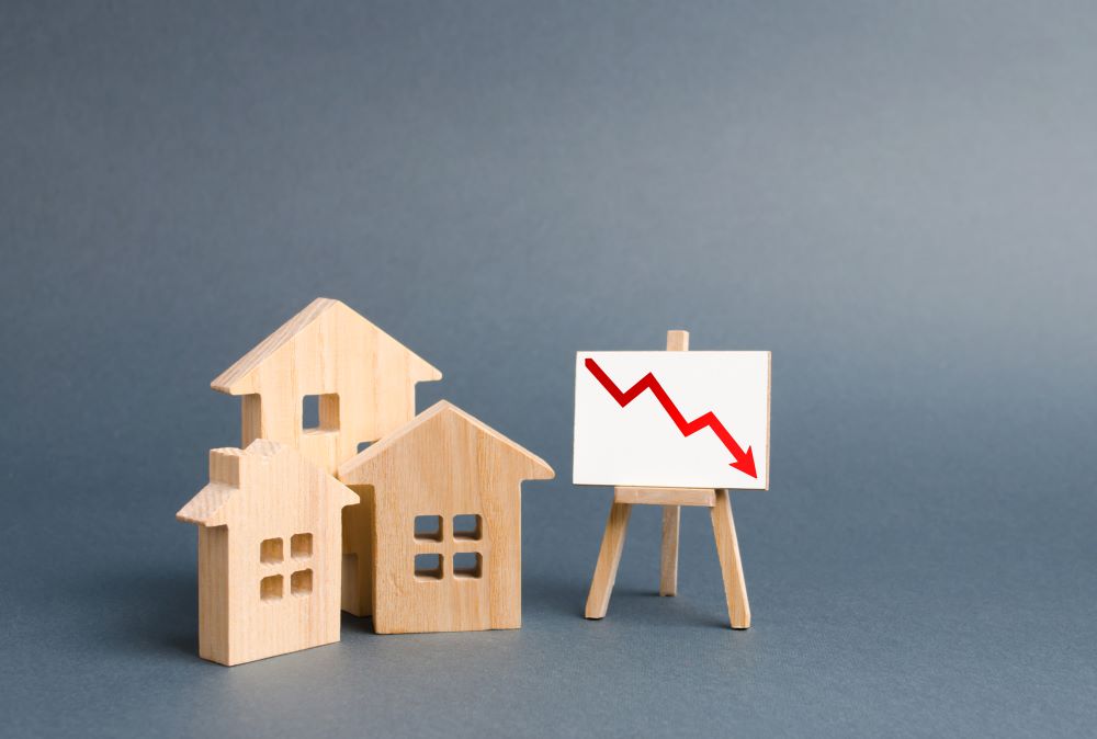 Three wooden houses and a poster with a symbol of declining property value indicated in a chart