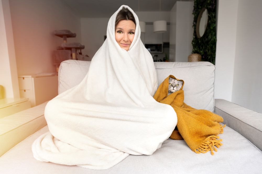 Woman feeling cold. Woman and cat warming under a blanket
