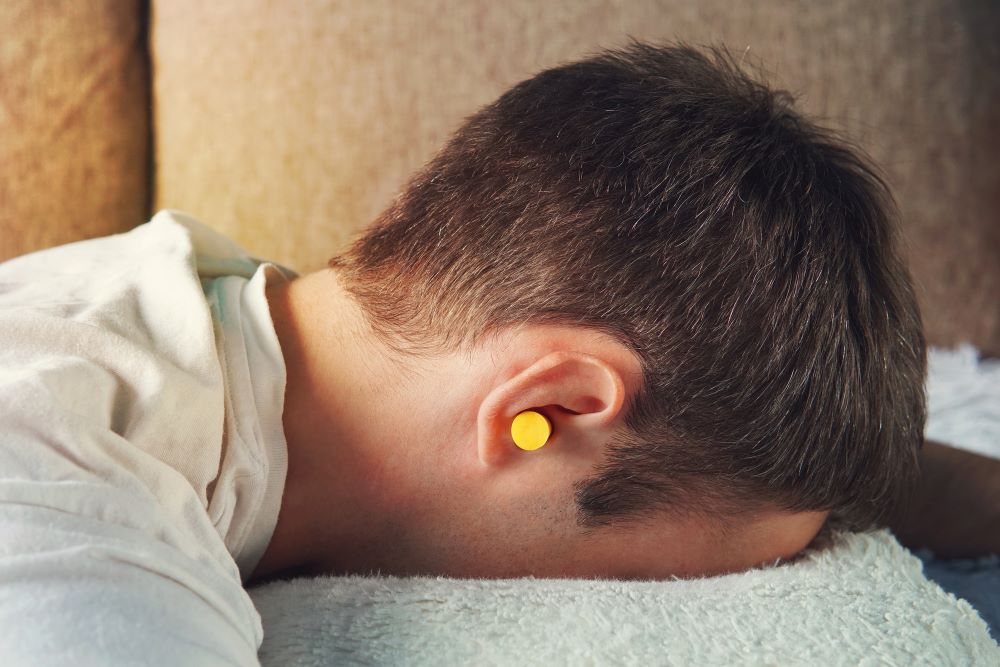 Young man wearing yellow ear plugs with his head pressed against a pillow