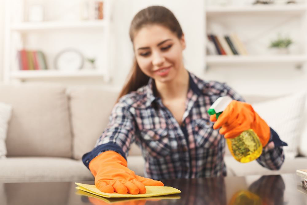 Woman using spray cleaner on wooden surface. Smiling girl cleaning furniture, housework and chores concept, copy space