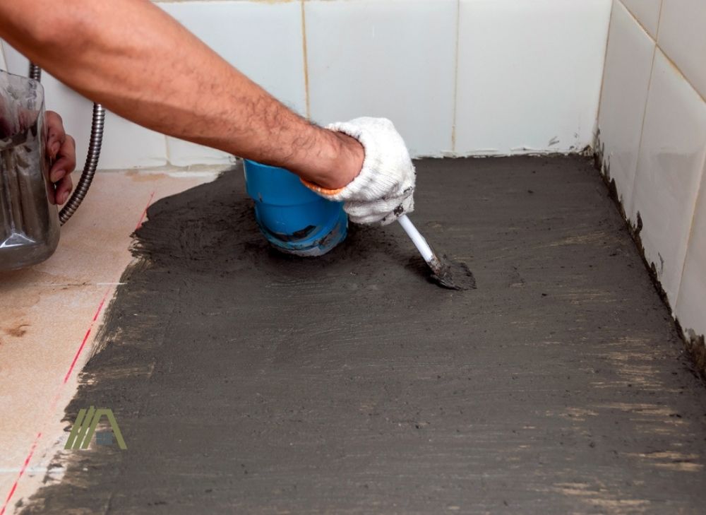 Construction workers are brushing waterproofing cement on tile floors in the bathroom. 