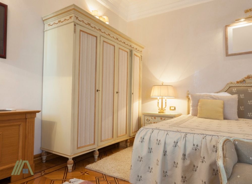 Old style white movable cupboard or armoires located inside a bedroom with a lamp and white bed