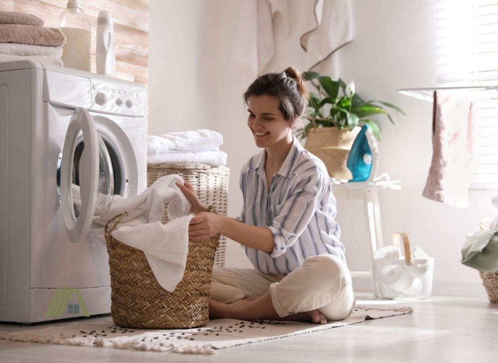 Young woman taking laundry out of washing machine at home 
