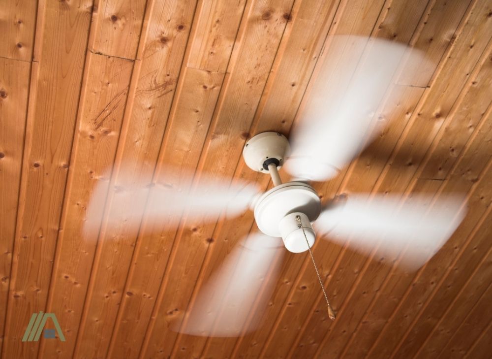 Rotating white four bladed ceiling fan with light installed in a wooden ceiling
