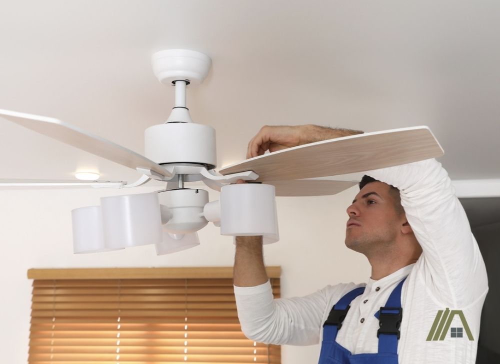 man fixing the unbalanced blade of a white ceiling fan