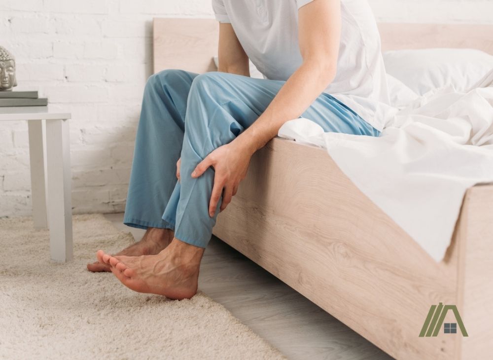 man sitting in bed touching his leg due to muscle ache