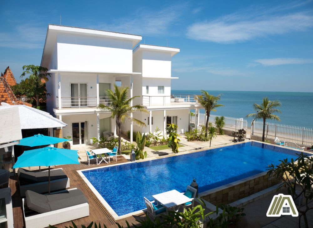 two story white concrete house and a pool in front of a beach
