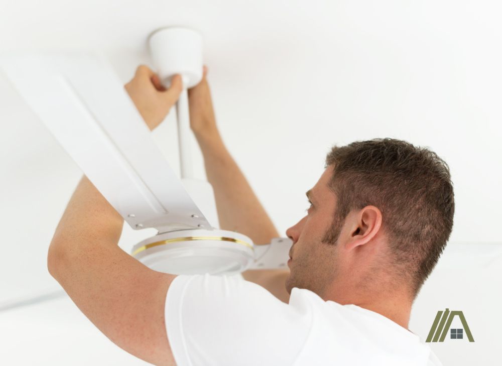 Man inspecting the downrod of a white ceiling fan