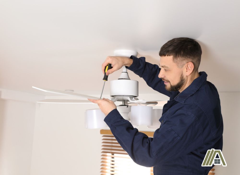 Man tightening the screw of the blade of a white ceiling fan