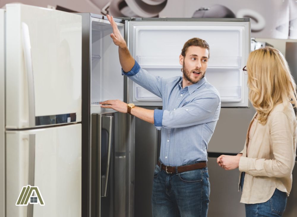 Man in suit checking refrigerator while talking to a blonde woman