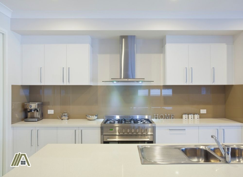 Modern clean kitchen with white cupboards and kitchen island, stainless steel range hood, stove, sink and coffee maker