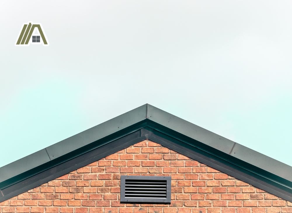 Black vent installed on a gable roof with a brick wall