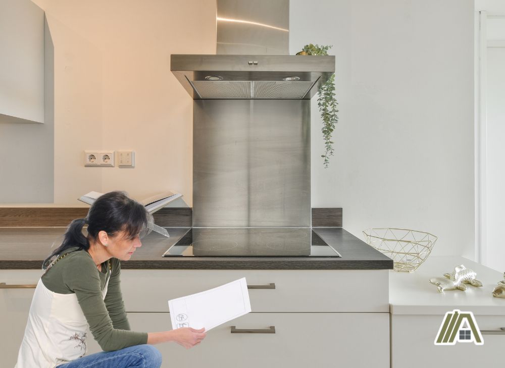 Woman reading a manual in front of a kitchen counter with an induction stove and a range hood