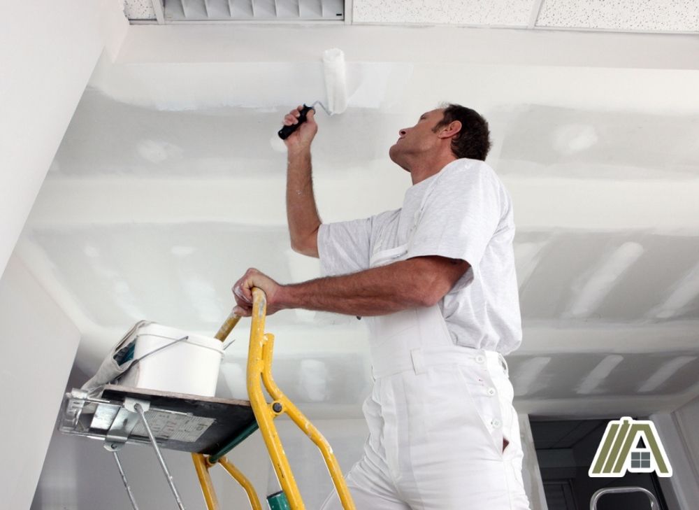 Man on a ladder painting the ceiling with white paint