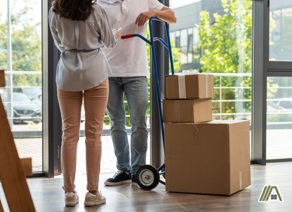 Woman holding a tablet in front of a delivery guy with a trolley full of packages