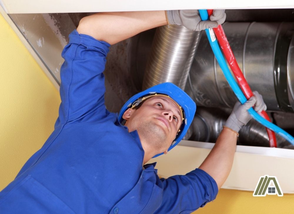 Man in PPE fixing pipes in ceiling filled with air ducts