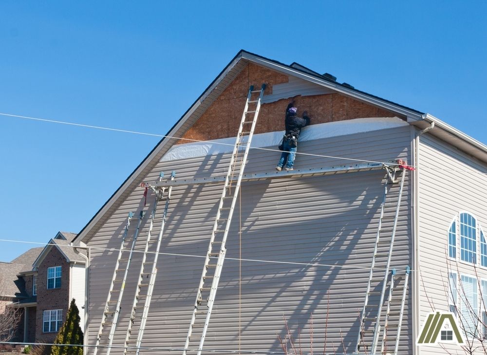 Man stepping on a ladder installing a cream colored shiplap on exterior wall