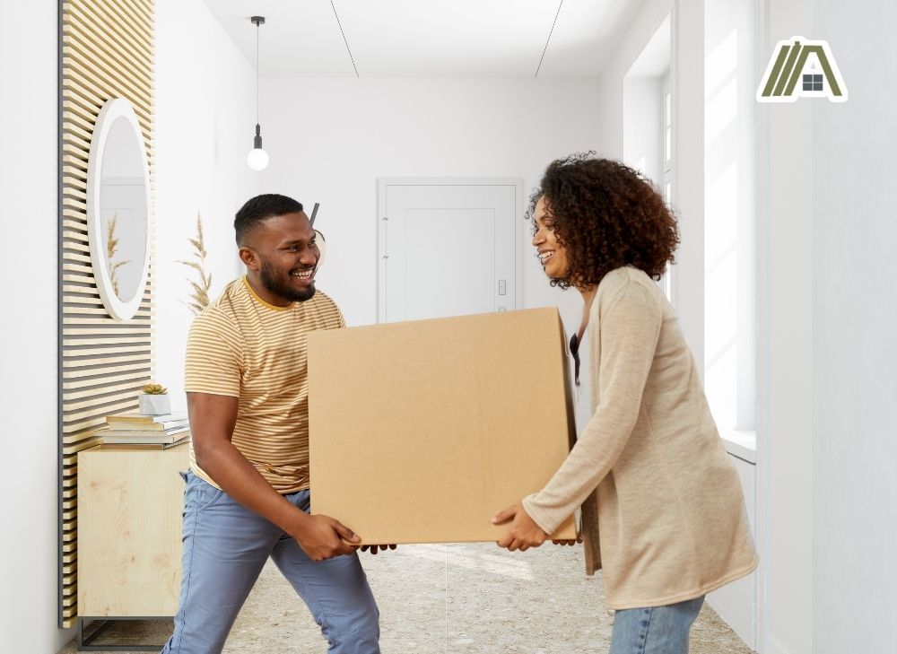Woman and man helping each other to carry a box inside the house