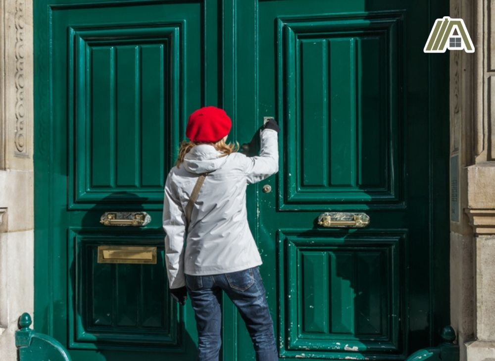 Woman with red hat knocking on a two large green doors