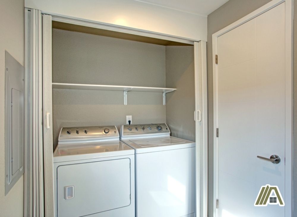 Two white gas dryers inside a closet with folding doors