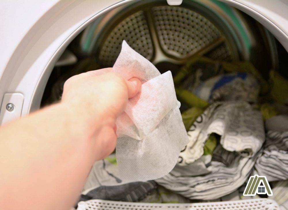 Woman placing a dryer sheet inside the dryer with clothes inside